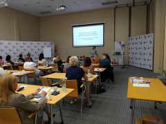 widok z tyłu sali na prowadzącego szkolenie pana Dariusza Szczotkowskiego, który stoi bokiem do kilkunastu uczestników szkolenia siedzących przy dwuosobowych stolikach w trzech rzędach, w tle widoczny ekran z prezentacją, Toruń, 21 września 2023 r.